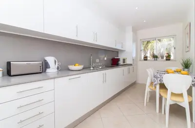 a kitchen with white cabinets and a table with chairs at Vilamoura Apartment Jacaranda - By Dalma Portuguesa in Vilamoura