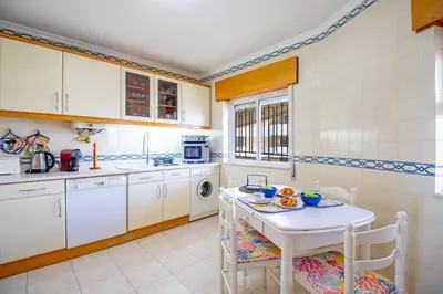 a kitchen with white cabinets and a white table and chairs at Apartamento Varandas do Sol in Vilamoura