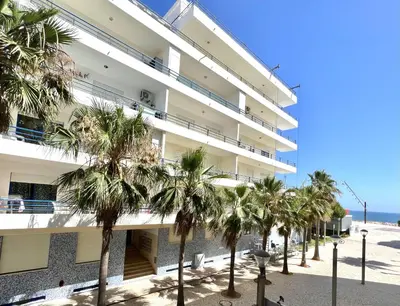 a large building with palm trees in front of it at Beachside Apartment - With Pool by HD PROPERTIES in Quarteira