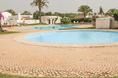 a swimming pool in a resort with palm trees and buildings at Villa Aldeia do Golf - BY BEDZY in Vilamoura