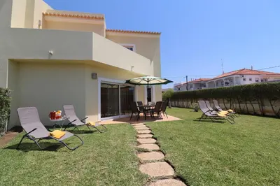 a group of chairs and an umbrella on a lawn at 3-Bed Townhouse with pool in Albufeira Balaia in Albufeira
