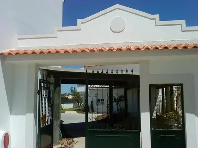 a white building with green doors and a gate at Lovely 1-Bedroom Apartment in Olhos de Agua in Albufeira