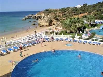 a large swimming pool with a beach and the ocean at Apartamentos Borda D´Agua in Albufeira