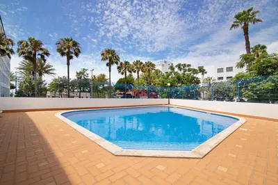 a large swimming pool with palm trees in the background at Pérola do Atlântico By the Sea in Quarteira