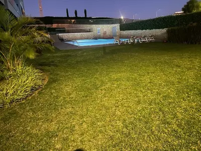 a lawn with chairs and a swimming pool at night at Albufeira Malpique Beach Apartment in Albufeira