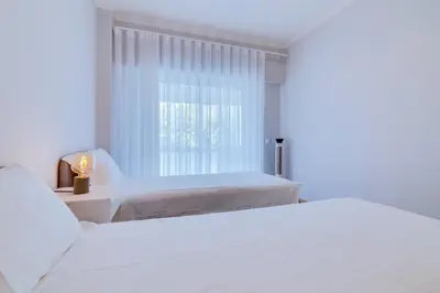 a white bedroom with two beds and a window at AL - Oceano T2 Frente Mar Quarteira in Quarteira