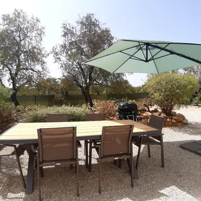 a wooden table with chairs and a green umbrella at Casa Aventura in Boliqueime