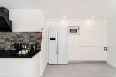 a white kitchen with a refrigerator and a counter at Privilege Deluxe Apartment Casa Mãe, Faro in Faro