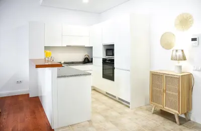 a kitchen with white cabinets and a table with a lamp at Beach Waves Apartment in Faro