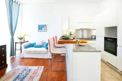 a kitchen and living room with white cabinets and a table at Jump Into the Lull Apartment in Faro