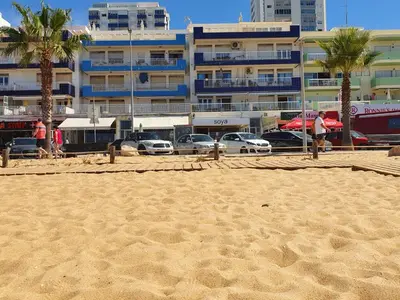 a sandy beach with cars parked in front of a building at T2-MAMAMIA II Frente Mar in Quarteira