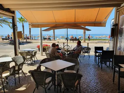 two people sitting at tables in a restaurant with the beach at T2-MAMAMIA II Frente Mar in Quarteira