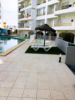 a swimming pool with an umbrella next to a building at 1 Bedroom Apartment Chaves, Praceta Vitorino Nemesio, Albufeira in Albufeira