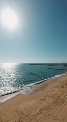 a beach with a person walking on the sand at Infante Sagres by FHR1º linha da praia in Quarteira