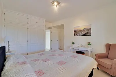 a white bedroom with a bed and a chair at Casa de Apra by Portucasa in Loulé