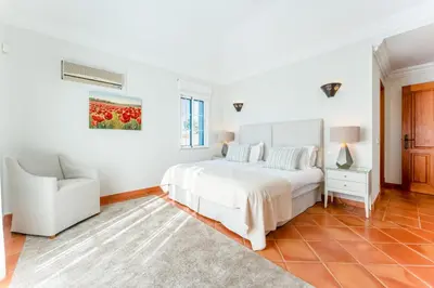 a white bedroom with a bed and a chair at Villa Breena - Quinta do Mar in Almancil