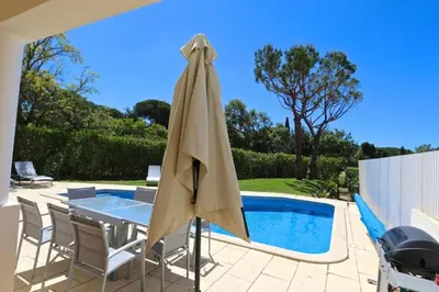 a patio umbrella and chairs next to a swimming pool at Spacious Vilamoura Villa 4 Bedrooms Villa Amendoeira Table Tennis in Quarteira