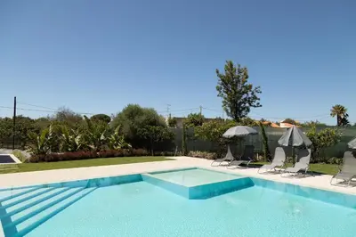 a swimming pool with two chairs and an umbrella at O Pinhal do Avô - BY BEDZY in Almancil