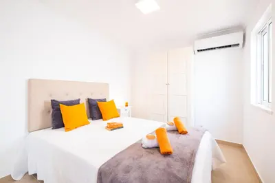 a white bedroom with a large white bed with yellow pillows at Casa Negril by Algarve Vacation in Albufeira