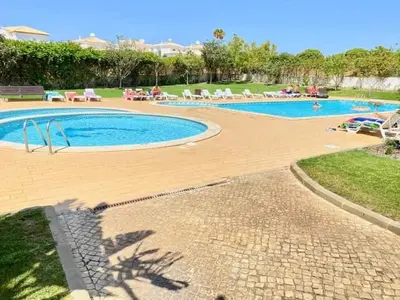 a swimming pool with chairs and people sitting around it at Flamingos Apartment with 2 swimming pool com check in e check out ao domingo em julho e agosto in Albufeira