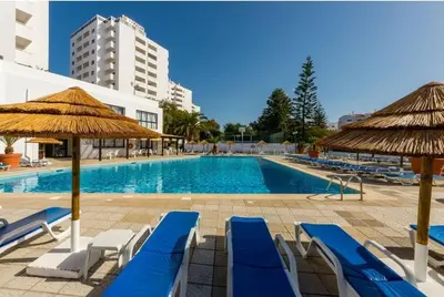 a swimming pool with blue lounge chairs and umbrellas at Albufeira SPOT com piscinas exteriores e interior! in Albufeira