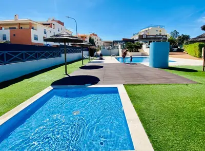 a blue swimming pool with green grass and buildings at Corcovada, Sunny and Bright T1 with Large Terrace, Albufeira in Albufeira