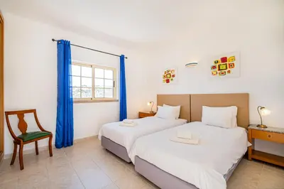 two beds in a room with a chair and a desk at Villa Duarte in Albufeira