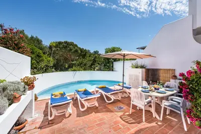 a patio with a table and chairs and a swimming pool at Victory Village Beach Villa - Quinta do Lago in Quinta do Lago