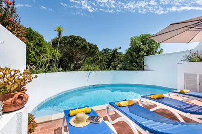 a swimming pool with blue chairs and an umbrella at Victory Village Beach Villa - Quinta do Lago in Quinta do Lago