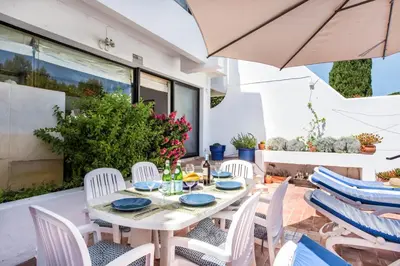 a table and chairs on a patio with an umbrella at Victory Village Beach Villa - Quinta do Lago in Quinta do Lago
