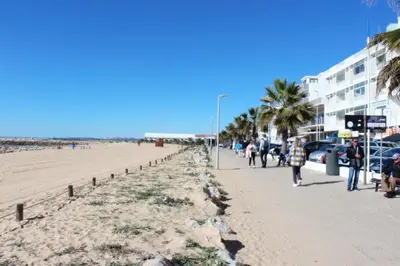 a beach with palm trees and people walking on the sidewalk at Quarteira Mar - Beach Front in Quarteira