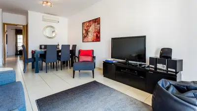 a living room with a television and a table with chairs at Central Albufeira 2-B Apt Sleeps 6 Pool Parking in Areias Sao Joao