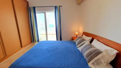 a bedroom with a blue bed with a large window at Quarteira Beach Vacation: 2BR steps to the sand in Quarteira