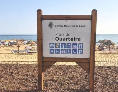 a sign on the beach in front of the ocean at Quarteira Beach Vacation: 2BR steps to the sand in Quarteira