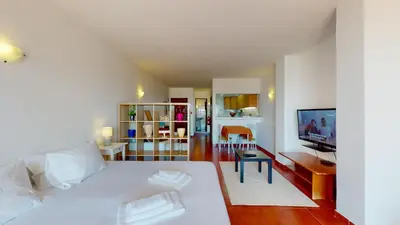 a bedroom with a white bed and a living room at Apartamento CPiscina-Albufeira in Albufeira