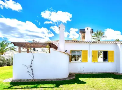 a white house with yellow shutters and a fence at Villa PACA Algarve Vilamoura 8 personnes in Quarteira