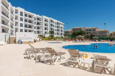 a swimming pool with chairs and a table and a building at Vista das Ondas - Apartamento 204 in Albufeira