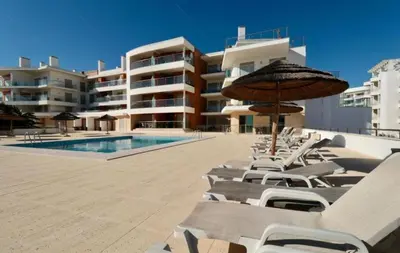 a group of lounge chairs and an umbrella next to a pool at Apartamento Varandas do Mar in Albufeira