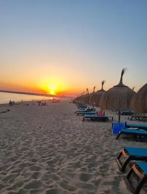 a beach with chairs and straw umbrellas at sunset at Eco Lodge Villa das Alfarrobas com Piscina in Algoz