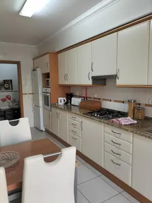 a kitchen with white cabinets and a table and chairs at T2 Infante AC wifi Garagem 50m Praia in Quarteira